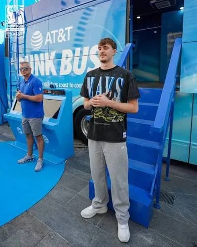 A tall young player in a Mavs tee stands by the blue AT&T Dunk Bus steps