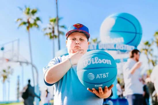 A young fan in a Superman cap holds an AT&T basketball in front of the Dunk District sign